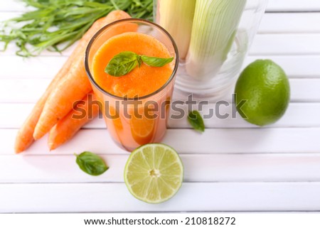 Glass of fresh carrot juice, spring onion, lime, tuft of grass and carrot on wooden background
