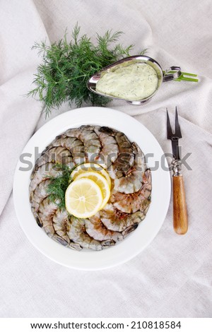 White round plate of prawns with dill, lemon and sauce on white tablecloth