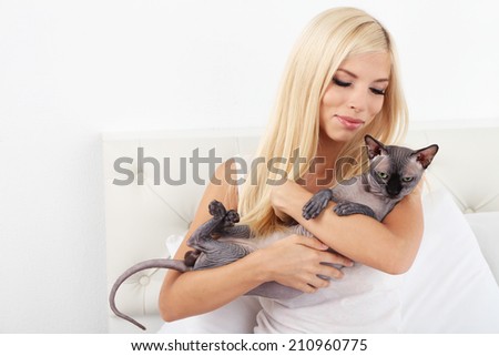 Beautiful young woman with gray sphinx cat sitting on bed