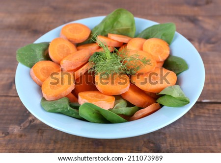 Slices of carrot, sorrel and dill in blue round bowl on wooden background