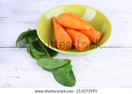 Carrots and sorrel in round green bowl on wooden background