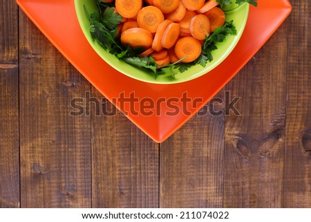 Slices of carrot, sorrel and parsley in green round bowl on wooden background