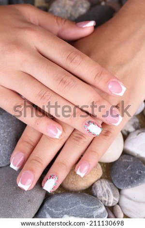 Female hand with stylish colorful nails on sea pebble background