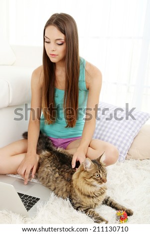 Beautiful young woman with cat sitting on carpet in room