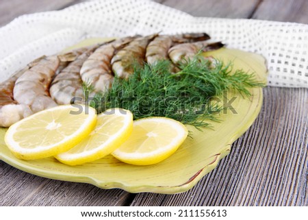 Square plate of prawns with dill and lemon on a yellow napkin on grey wooden background