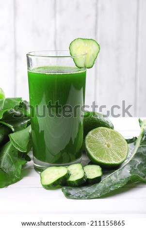 Lime juice, slices of cucumber halves of lime on wooden table in front of wooden wall