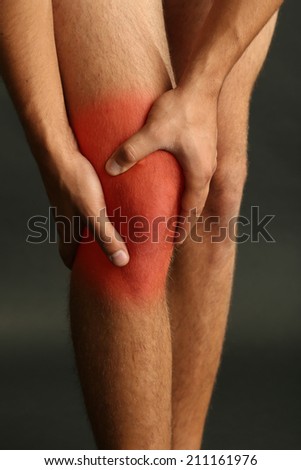 Pain concept. Young man with knee pain on dark background