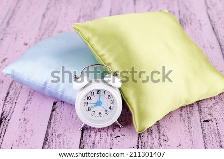Plastic clock on a silk pillows on wooden background