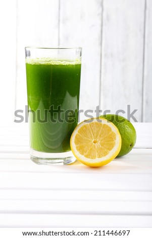Lime juice and halves of lime and lemon on wooden table in front of wooden wall
