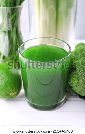 Glass of fresh lime juice, lime, slices of cucumbers and vase of grass on the table in front of wooden wall
