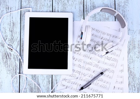 Tablet, printed music and earphones on wooden background