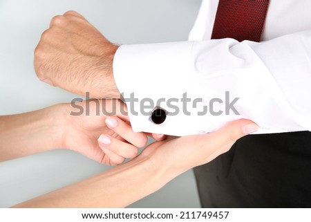 Woman helping man to do collar button up on grey background