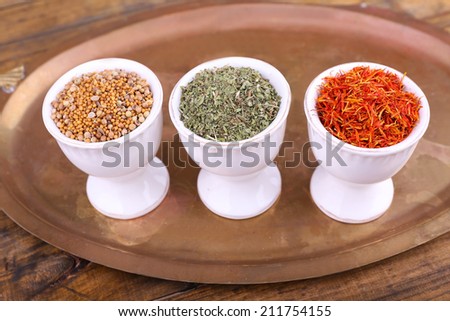 Small round tea bowls with different seasoning on a metal round tray on wooden background