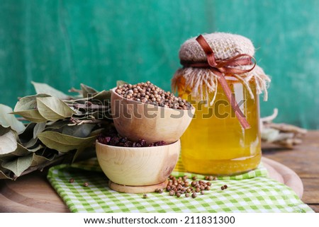 Round wooden bowls of seasoning, bay leaves and a glass bottle of honey on a green napkin on a tray on wooden background