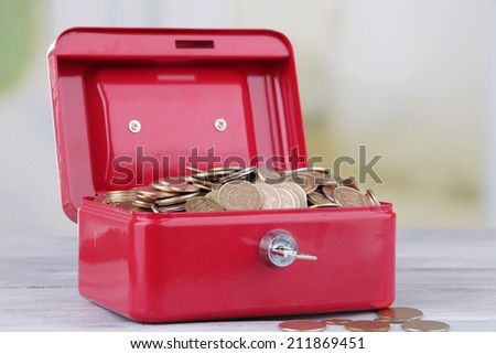 Rectangular red open suitcase with Ukrainian coins on wooden table