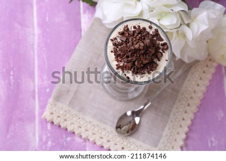 Yogurt, with chocolate cream, chopped chocolate and muesli served in glass on color  wooden background