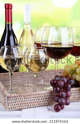 Bottles and glasses of wine and ripe grapes on table on natural background