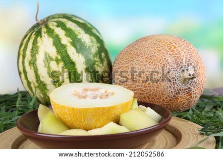 Melon and watermelon on brown plate on bamboo plate on grass on natural background