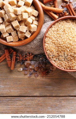 Brown sugar cubes, reed and crystal sugar in bowl with spices on wooden background