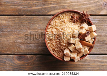 Brown sugar cubes and crystal sugar in bowl on wooden background