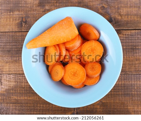 Slices of carrot in blue round bowl on wooden background