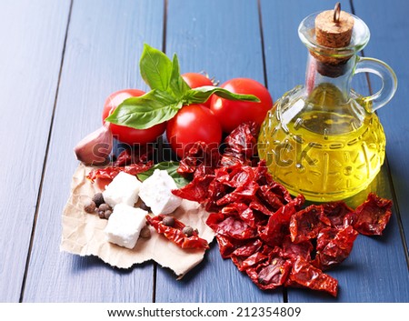 Sun dried tomatoes in glass jar, olive oil in glass bottle and feta cheese on color wooden background