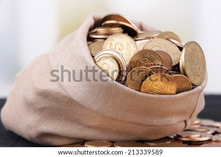 Fabric bag full of Ukrainian coins on wooden background