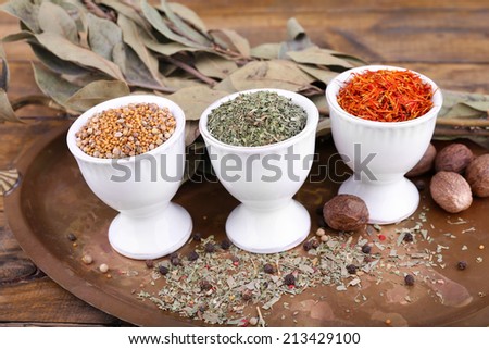 Small round tea bowls with different seasoning and bay leaves on a metal round tray on wooden background