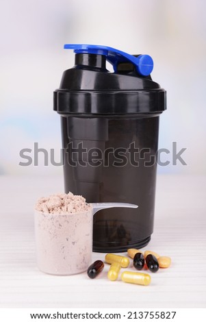 Whey protein powder in scoop with vitamins and plastic shaker on table on bright background