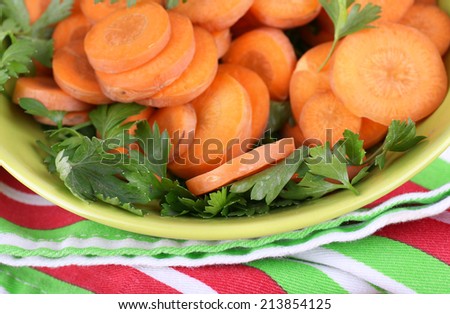 Slices of carrot, sorrel and parsley in green round bowl on napkin on wooden background