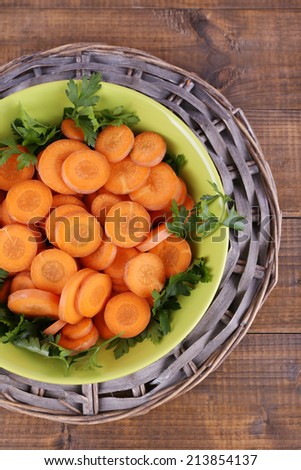 Slices of carrot, sorrel and parsley in green round bowl on wicker met on wooden background