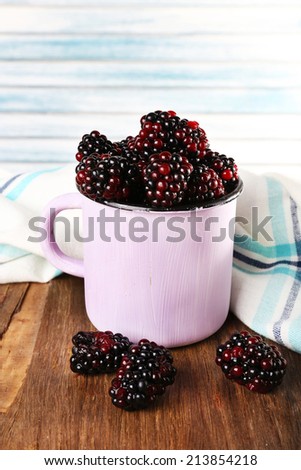 Metal mug of blackberries on napkin on wooden table on light background