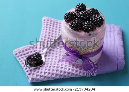 Healthy breakfast - yogurt with  blackberries and muesli served in glass jar, on color wooden background
