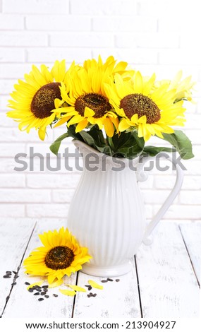 Beautiful bouquet of sunflowers in pitcher on table on brick wall background