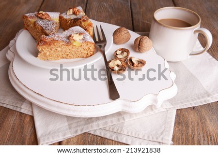 Pieces of delicious cake with nuts on wooden stand on table close up