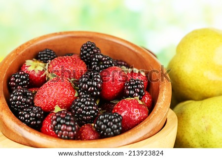 Berries in bowl with pears on table on bright background