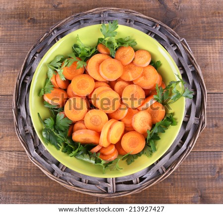 Slices of carrot, sorrel and parsley in green round bowl on wicker met on wooden background