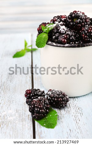 Metal mug of blackberries on wooden table on light background