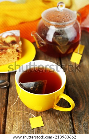 Cup with tea, teapot and tea bags on wooden table close-up