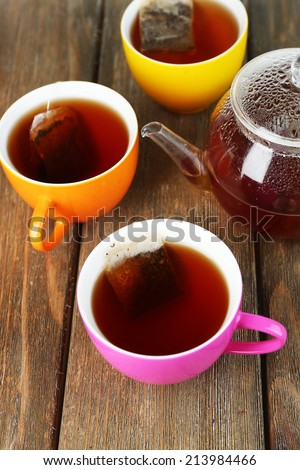 Cups of tea, teapot and tea bags on wooden table close-up