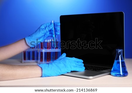 Scientist entering data on laptop computer with test tubes in a laboratory on blue background