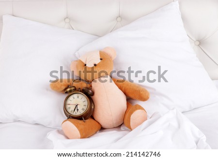 Metal clock and toy bear on pillows on a big white bed