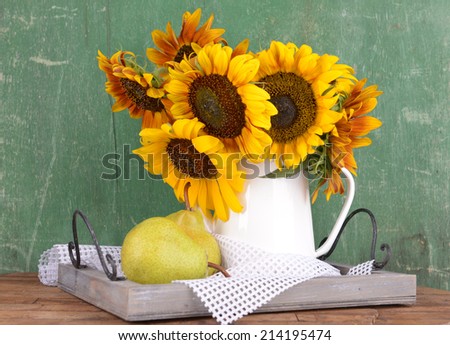 Beautiful sunflowers in pitcher with pears on table on wooden background
