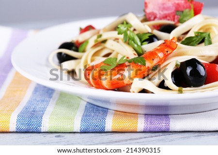 Fresh prawns with spaghetti, olives, tomatoes and parsley in a big round plate on a napkin on wooden table on grey background