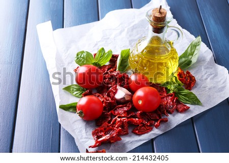 Sun dried tomatoes in glass jar, olive oil in glass bottle, basil leaves on color wooden background