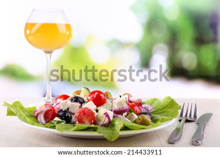 Greek salad in plate and glass of wine on wooden table on natural background