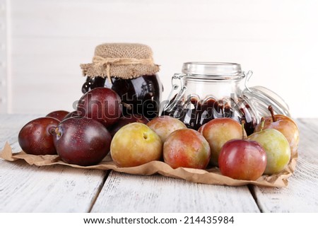 Plum jam and fresh plums in glass dish on piece of paper on wooden table on light background