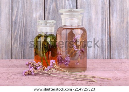 Bottles of herbal tincture and brunch of flowers on a wooden table in front of wooden wall