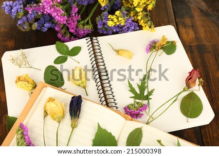 Composition with flowers and dry up plants on notebooks on table close up