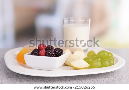 Slices of fruits with crispbreads and glass of milk on plate on table on bright background